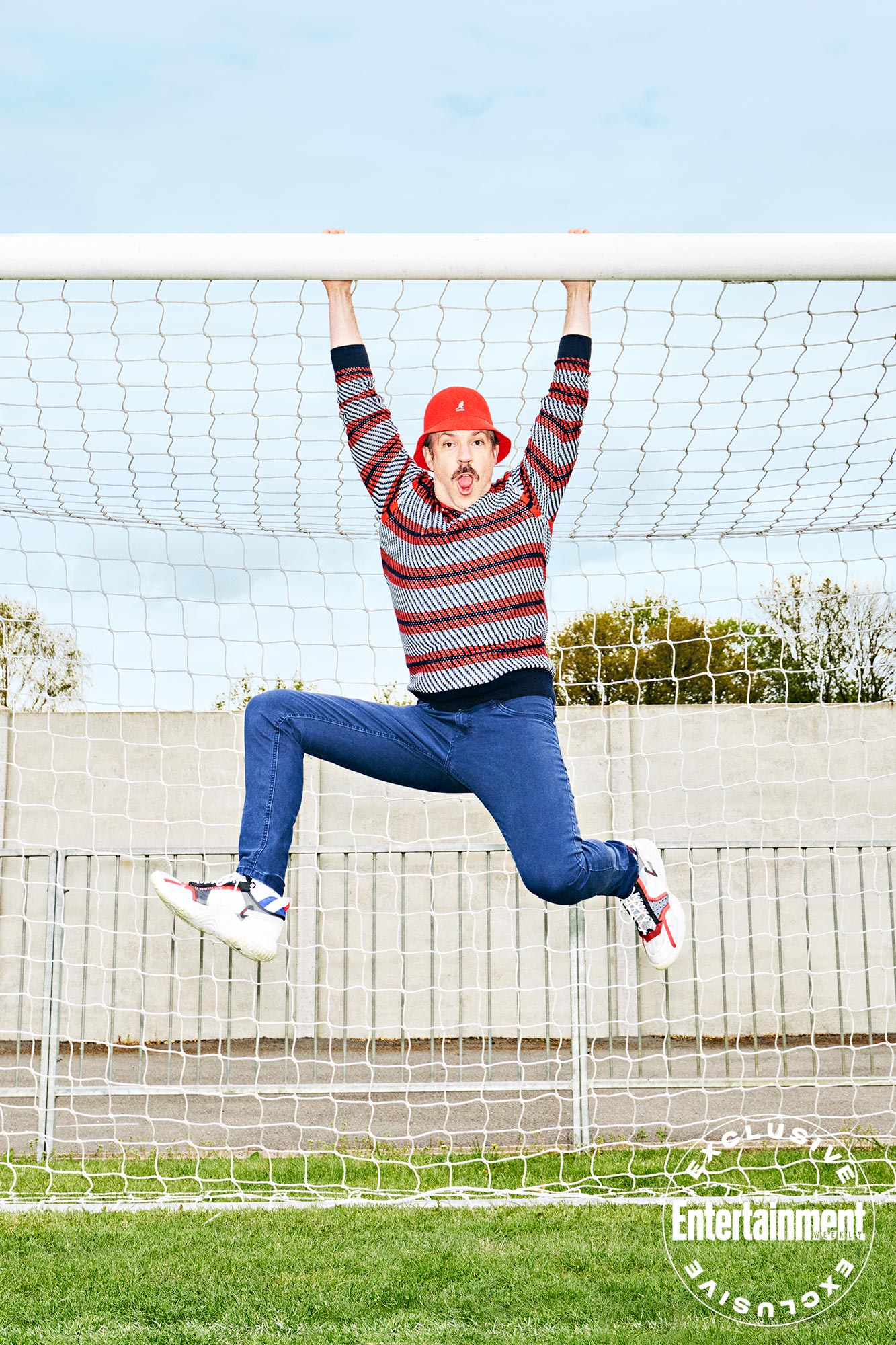 Jason Sudeikis hanging from goal post wearing red Kangol hat